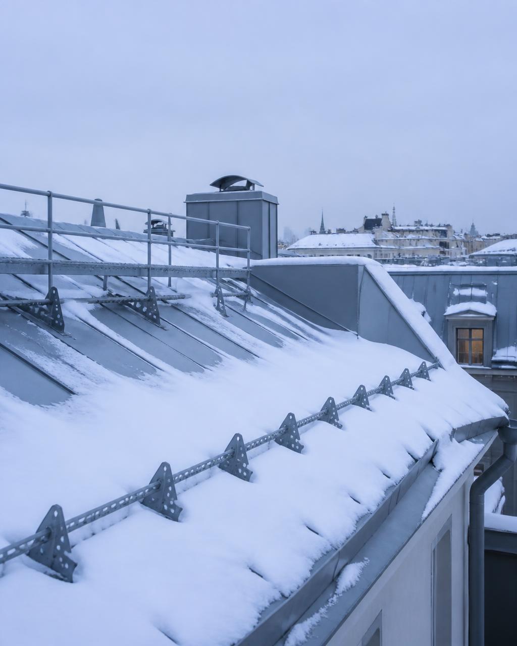 Snötäckt plåttak med snörasskydd och taksäkerhetsräcke i Stockholm
